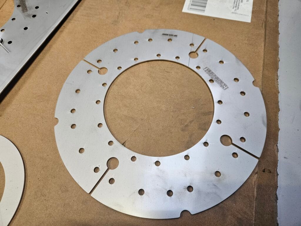 Cięcie stali laserem fiber Aktona: okrągły element metalowy z wycięciami. Napis: BMW 540 USA.